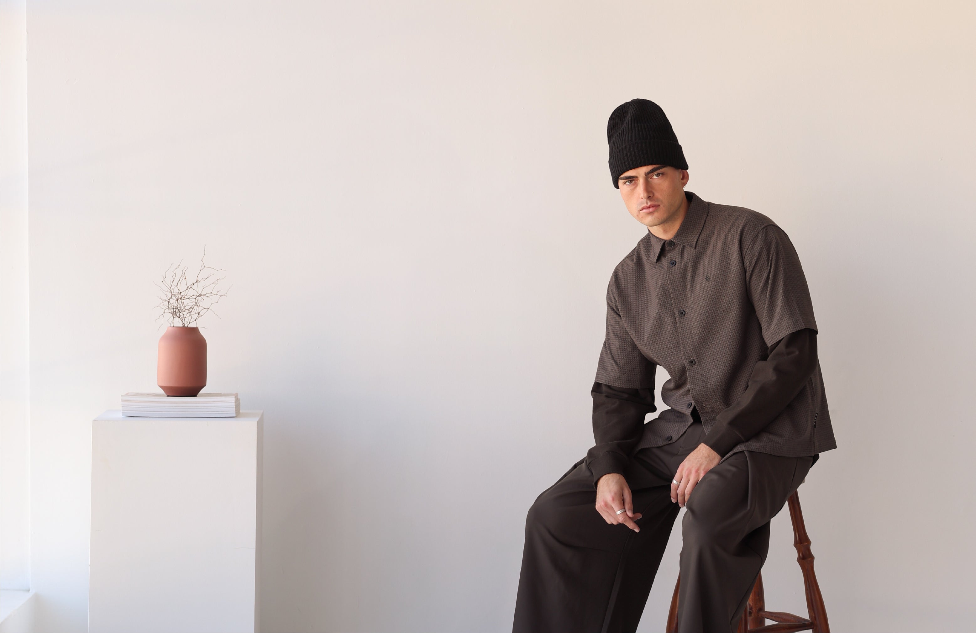 Person sitting on a stool next to a decorative plant and vase.
