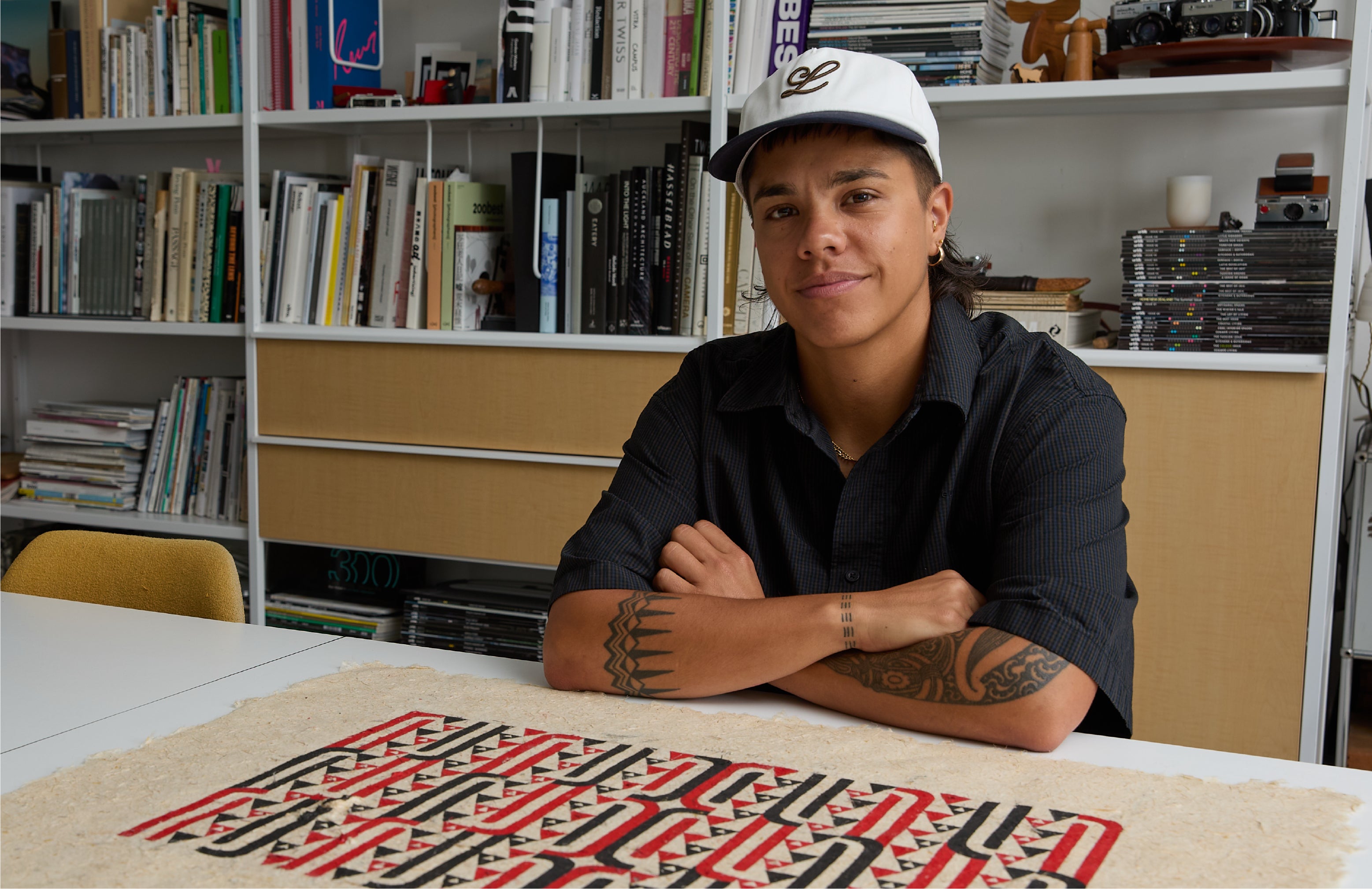 Person sitting at a table with a patterned artwork in a studio.