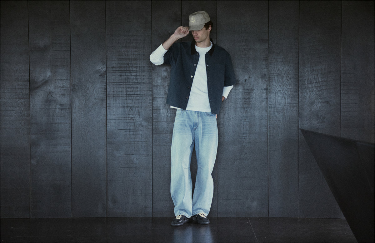 Person standing in casual attire against a dark wooden background.